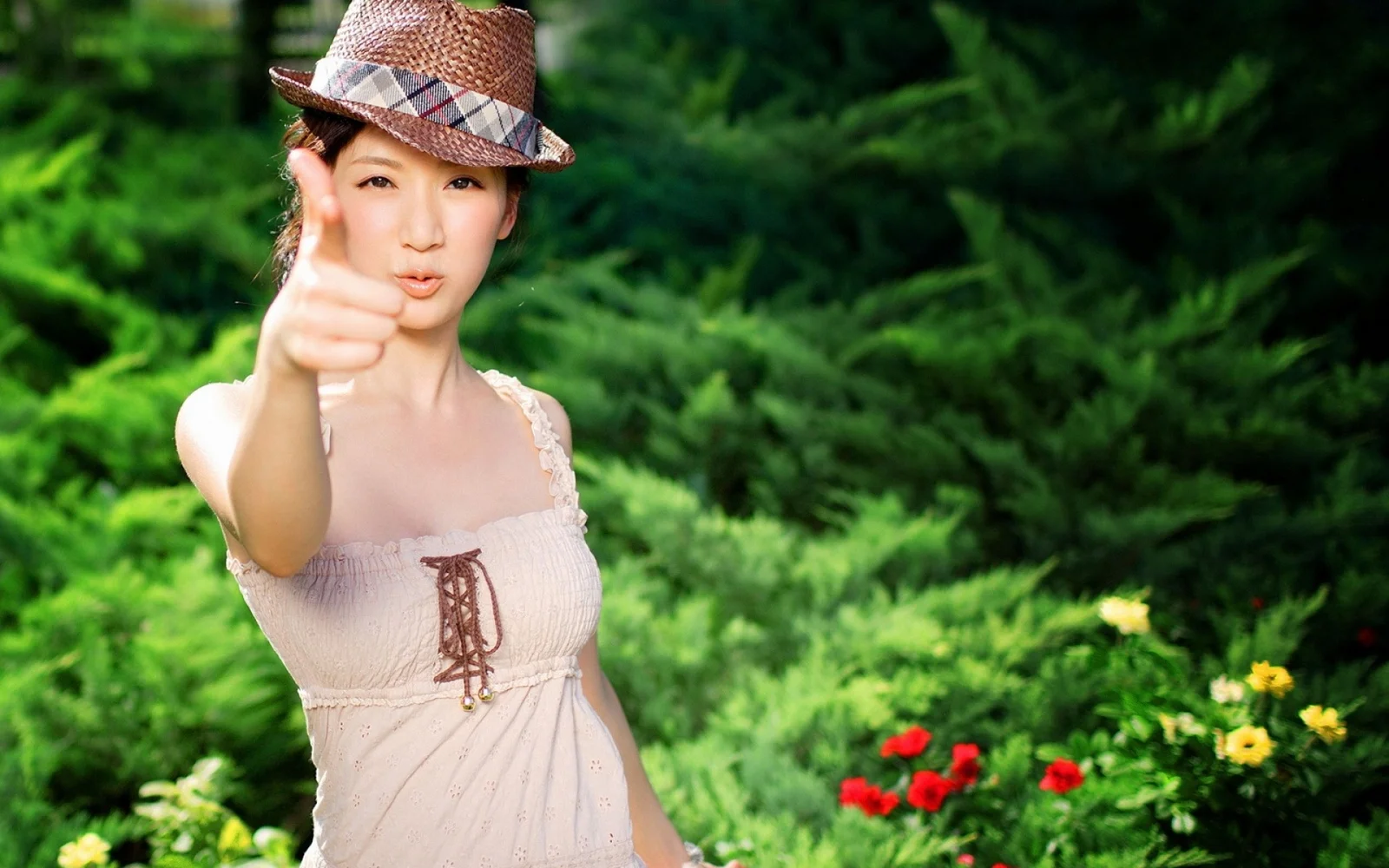 모자를 쓴 여성이 꽃이 피어 있는 푸른 정원에서 엄지손가락을 세우고 있습니다.