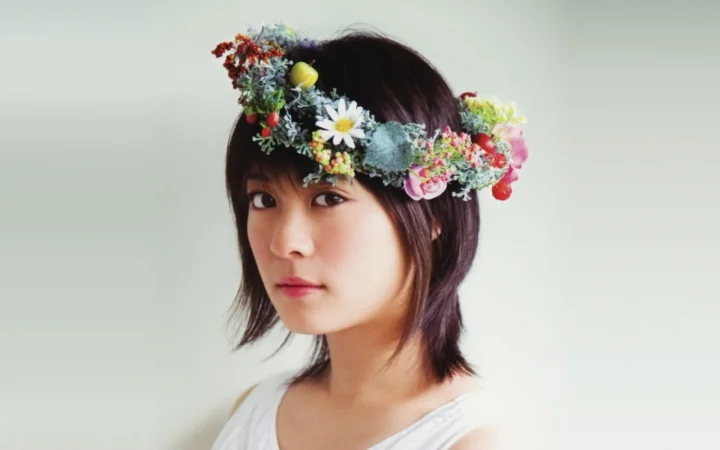 화려한 꽃관을 쓴 성인 여성이 밝은 배경 앞에서 카메라를 바라보고 있습니다.