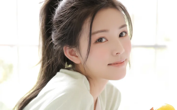 一位深色马尾、身穿浅色上衣的女性在明亮窗边回眸微笑。