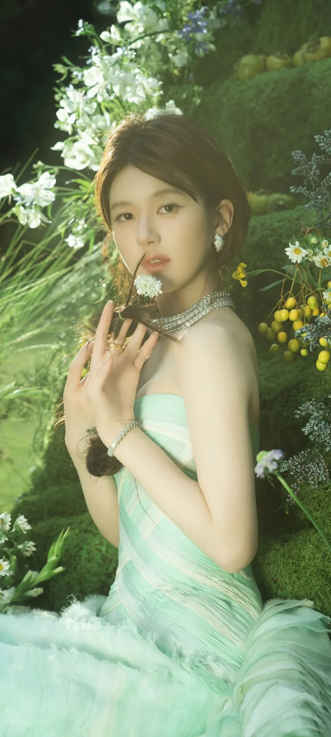 一名女性身穿薄荷绿色礼服，在繁花绿植环绕的花园中摆姿势。