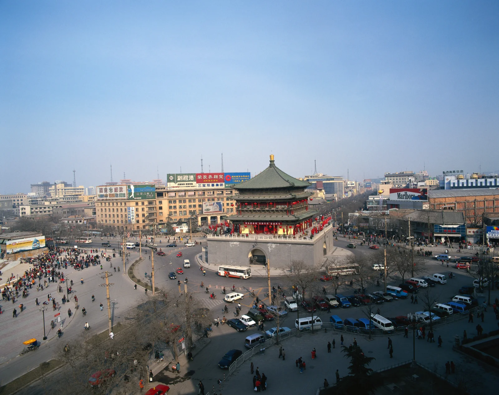 一座古建筑矗立在繁忙的城市广场中央，周围环绕着街道、车辆和行人。