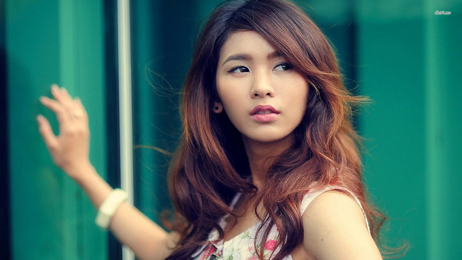 一名长发女性站在绿色玻璃背景前，侧头望向一旁。