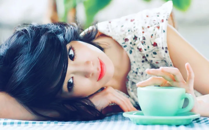 一名女性侧躺在桌面旁，手边放着一杯咖啡。