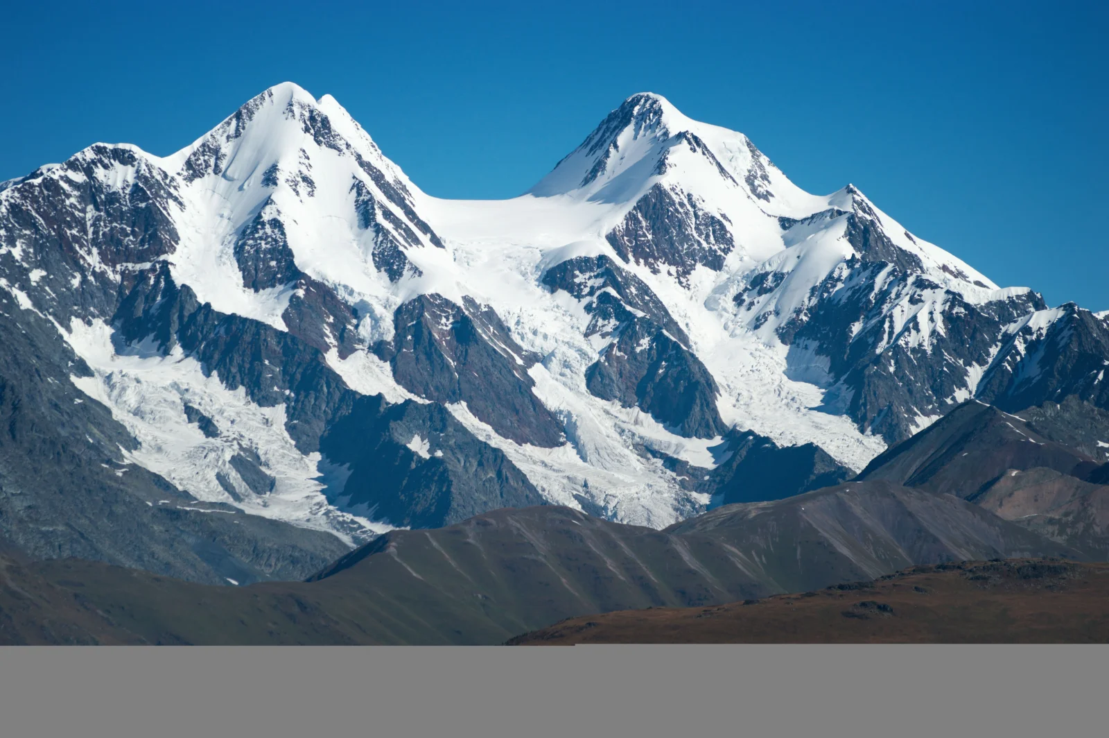 蓝天下的雪山、冰川和深色山脊构成壮丽的自然风景。