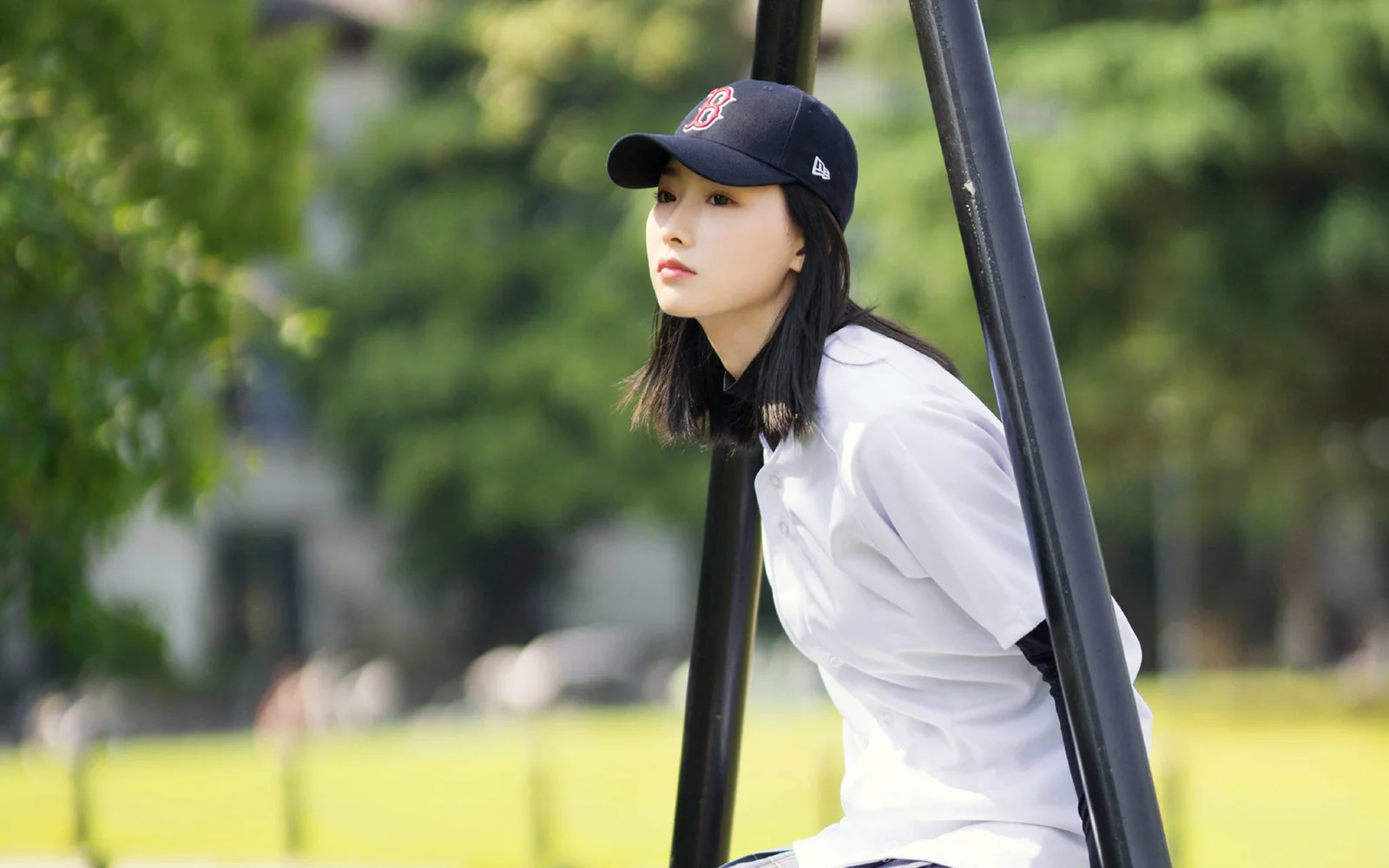 야구 모자와 흰색 셔츠를 착용한 여성이 야외 녹지 옆에서 앞을 바라보고 있습니다.