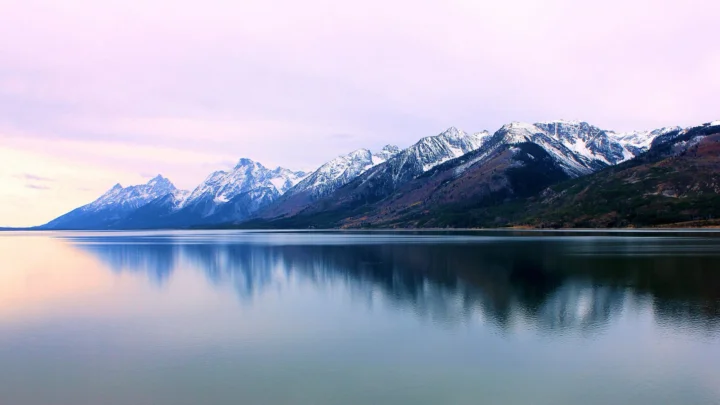 雪山沿湖延伸，宁静湖面映出山峦与淡紫色天空。