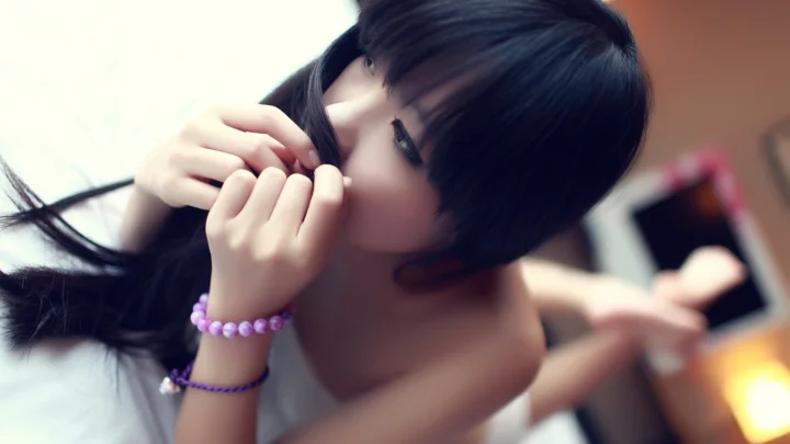 一名黑发女性侧脸靠近镜头，手持发丝，手腕上戴着紫色串珠手链。