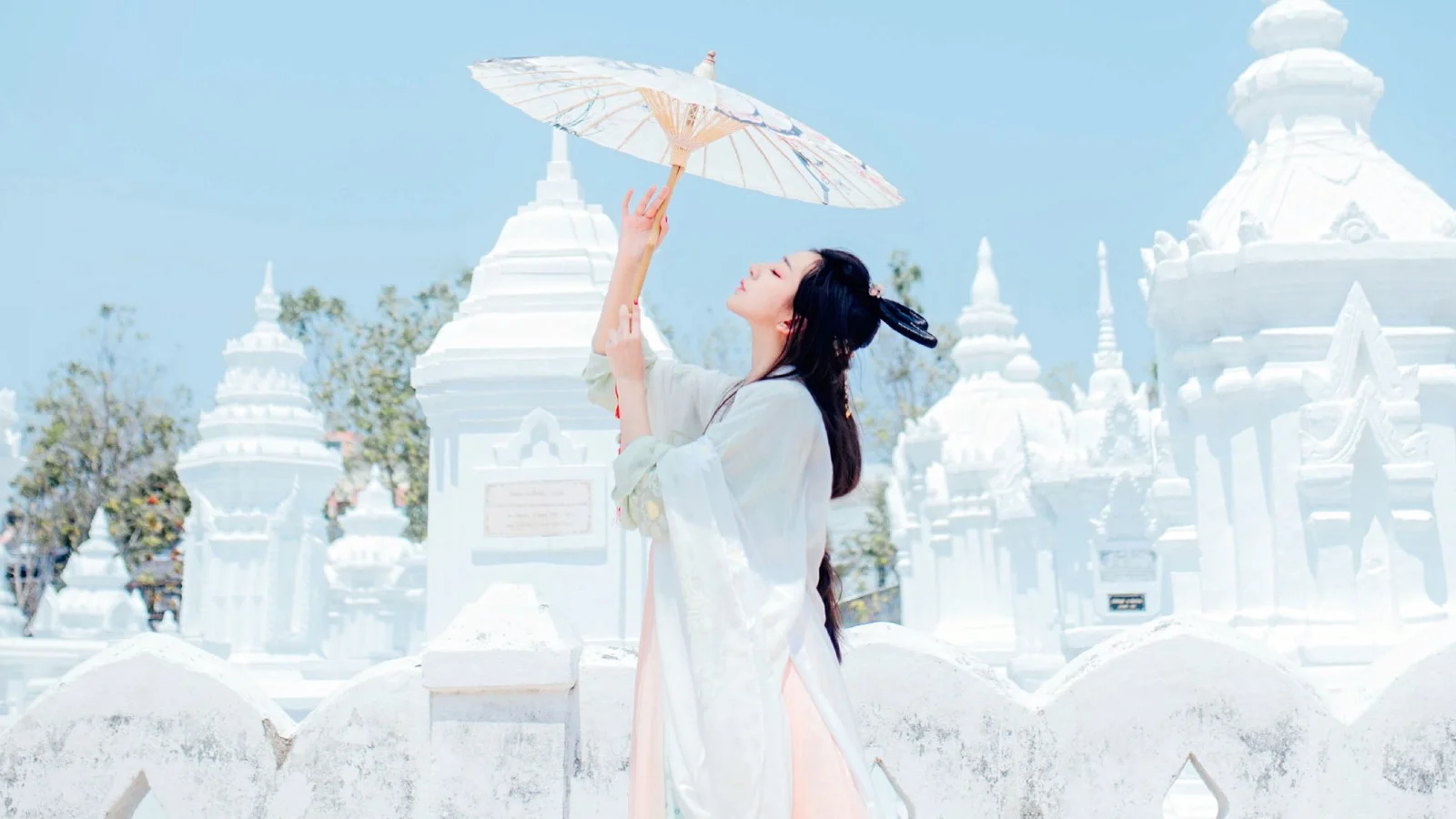 一名女子在蓝天下的白色寺院建筑间撑着一把伞。