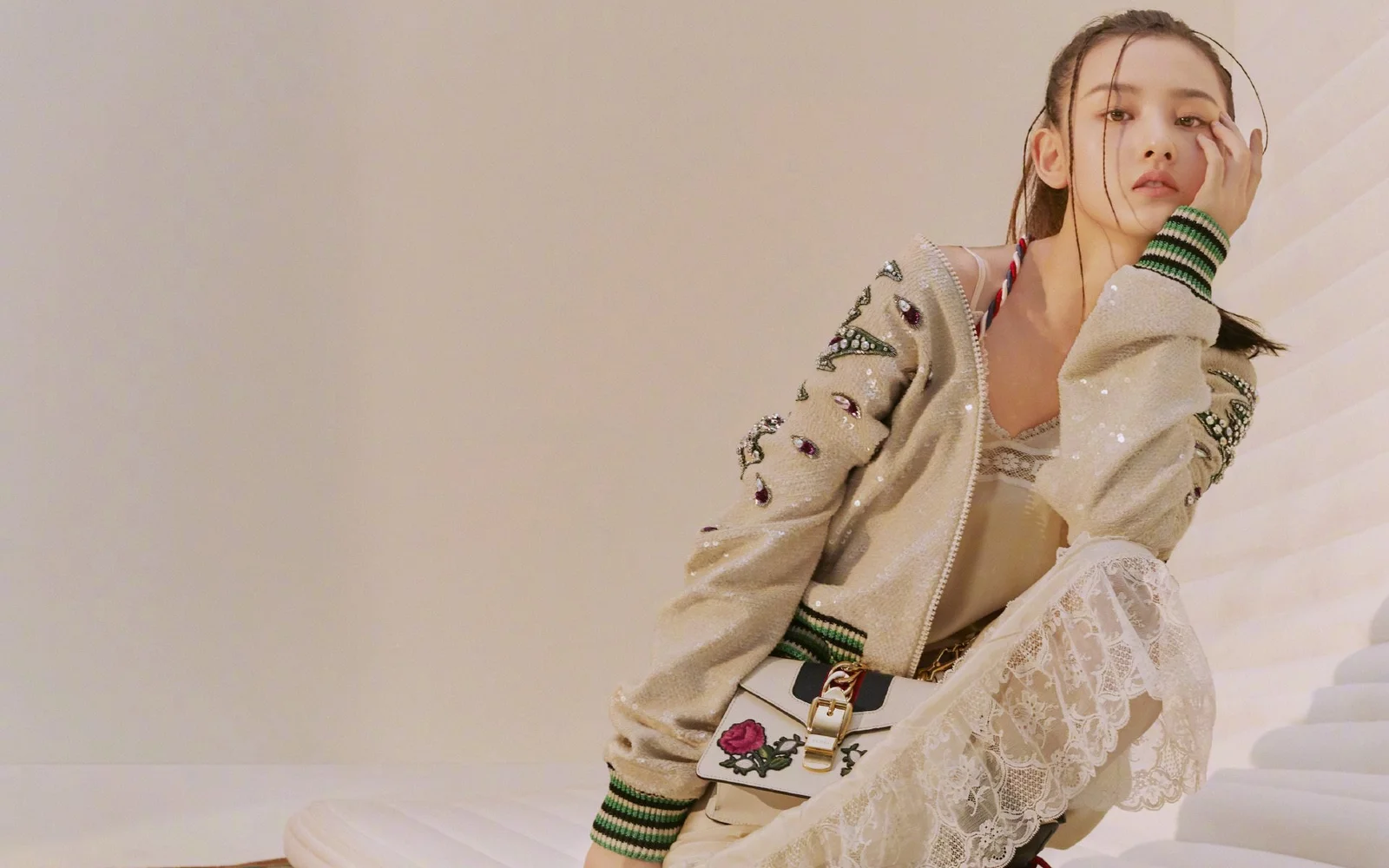 一位穿着装饰夹克和蕾丝服装的女性坐在室内白色阶梯旁。