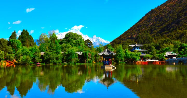碧蓝天空下，湖面倒映着山林、亭台与远处的雪山。