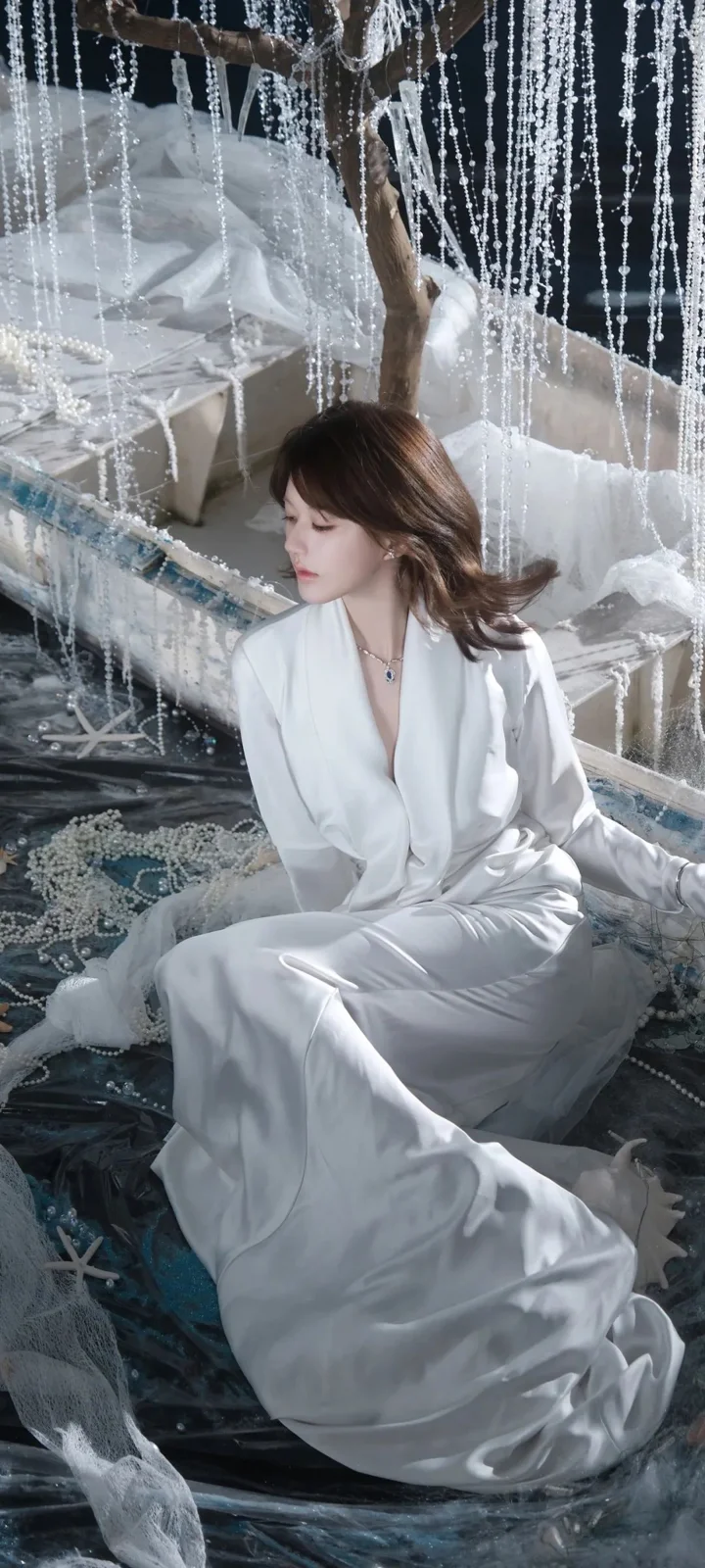 一名成年女性身穿白色长裙，坐在珠帘装饰的室内场景中。