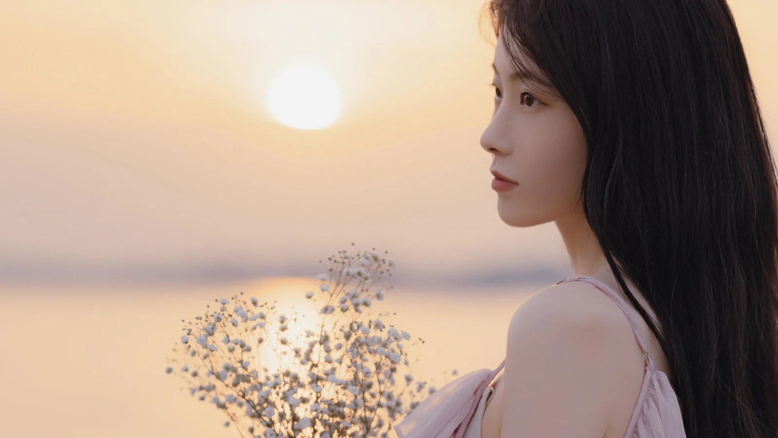 一名长发女子在夕阳和海面前的侧面肖像。