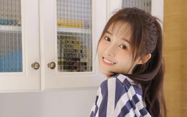 포니테일과 줄무늬 상의를 입은 여성이 실내에서 뒤돌아보며 미소 짓고 있다.