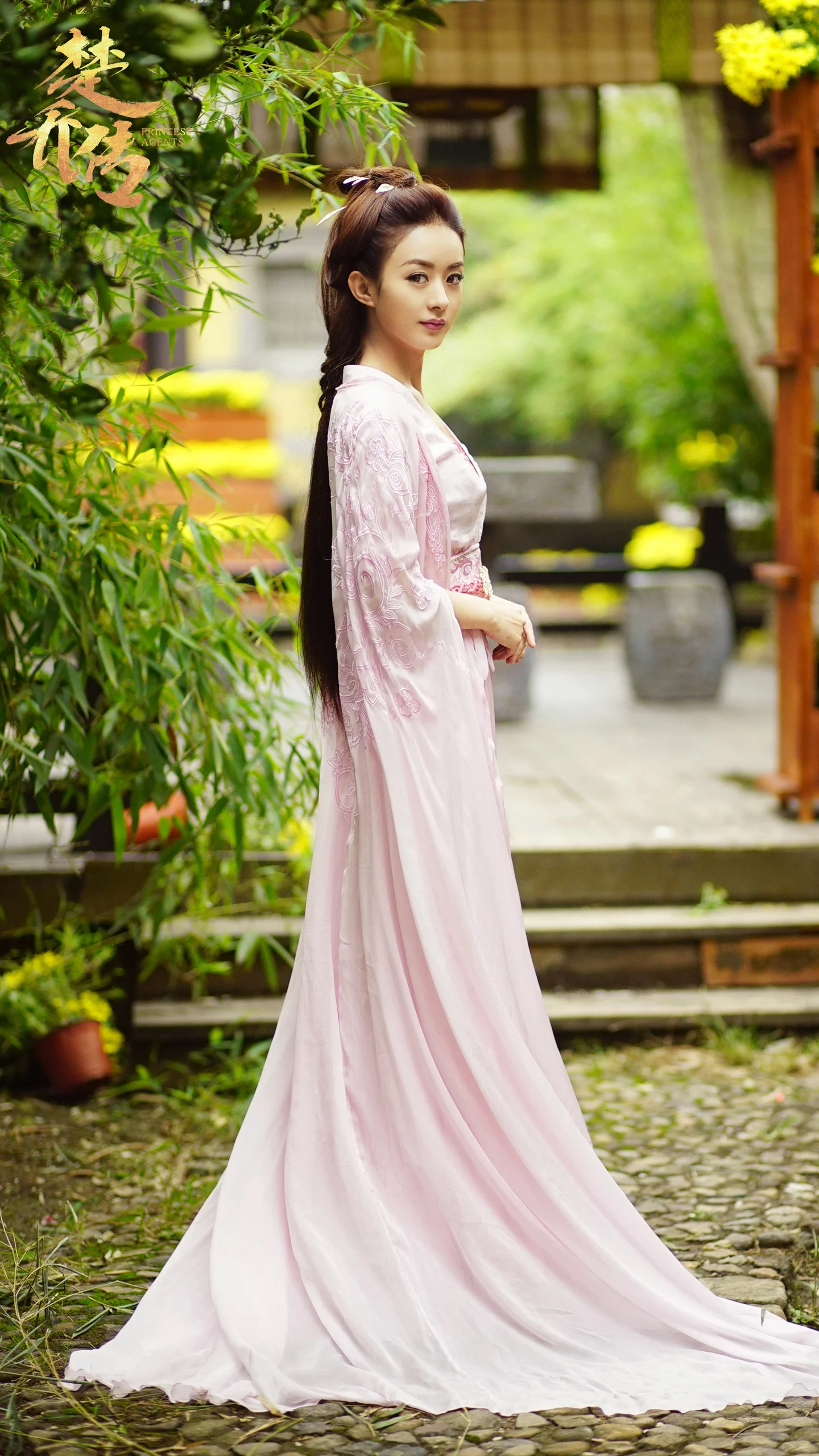 一名身穿粉色传统服饰的女子站在竹子环绕的庭院小径旁。