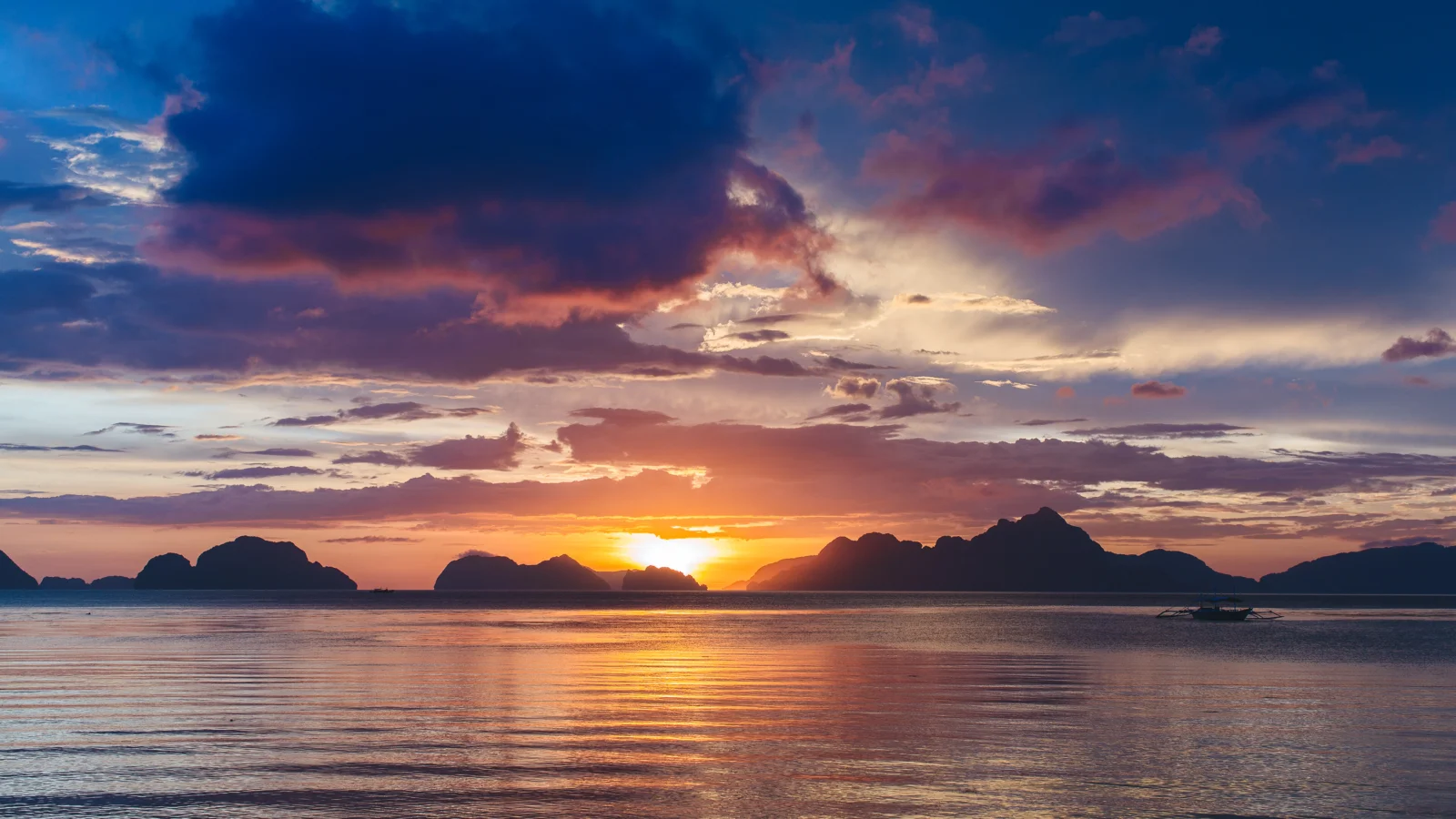夕阳沉入海平面，远处岛屿与云层在水面倒影中形成宁静的海景。