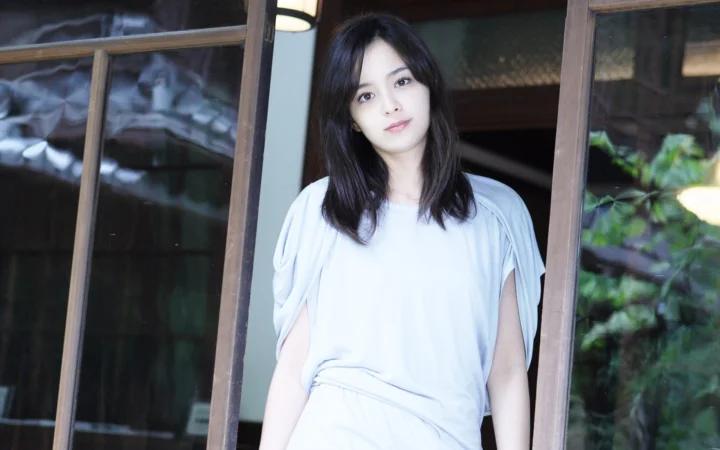 一名成年女性站在木质窗框旁，面向镜头微笑。