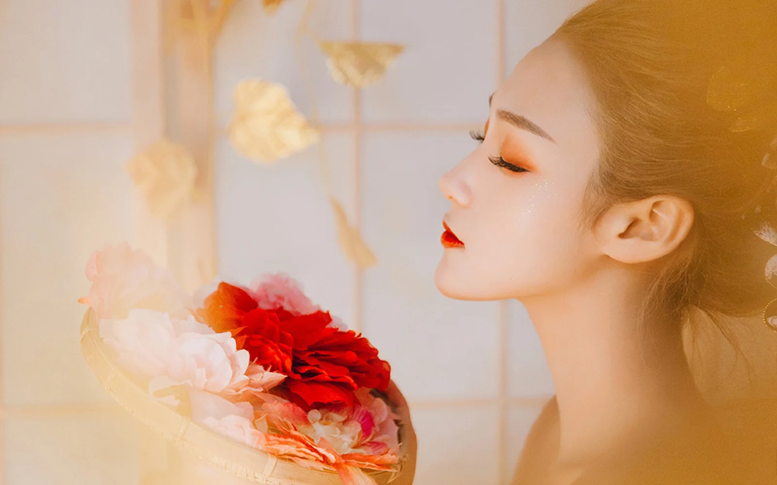 一位女性以侧脸面对镜头，手捧红色与浅色花朵组成的花束，画面笼罩在柔和暖光中。