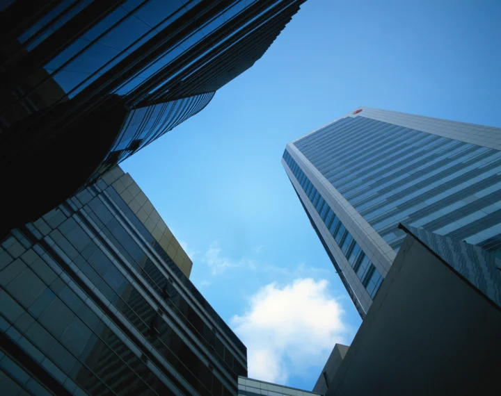 从低角度仰望多座现代玻璃建筑，蓝天和白云位于建筑之间。
