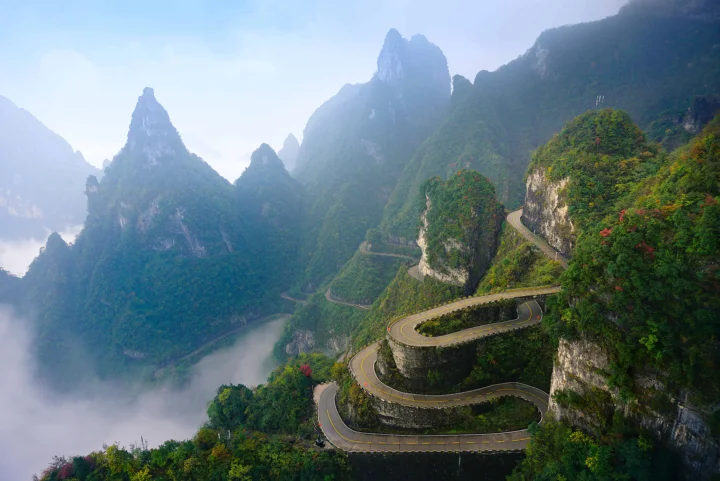 云雾缭绕的群山间，一条盘山公路沿着陡峭的绿色山壁蜿蜒而行。