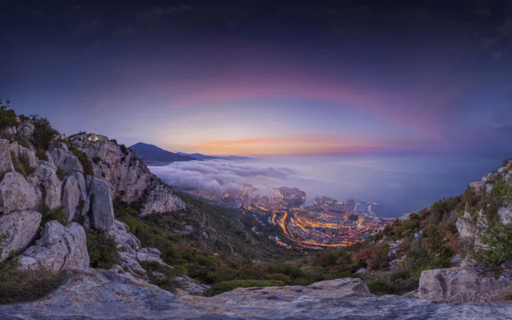 夕阳映照下的山间悬崖、云海与远处灯火构成壮丽的暮色风景。