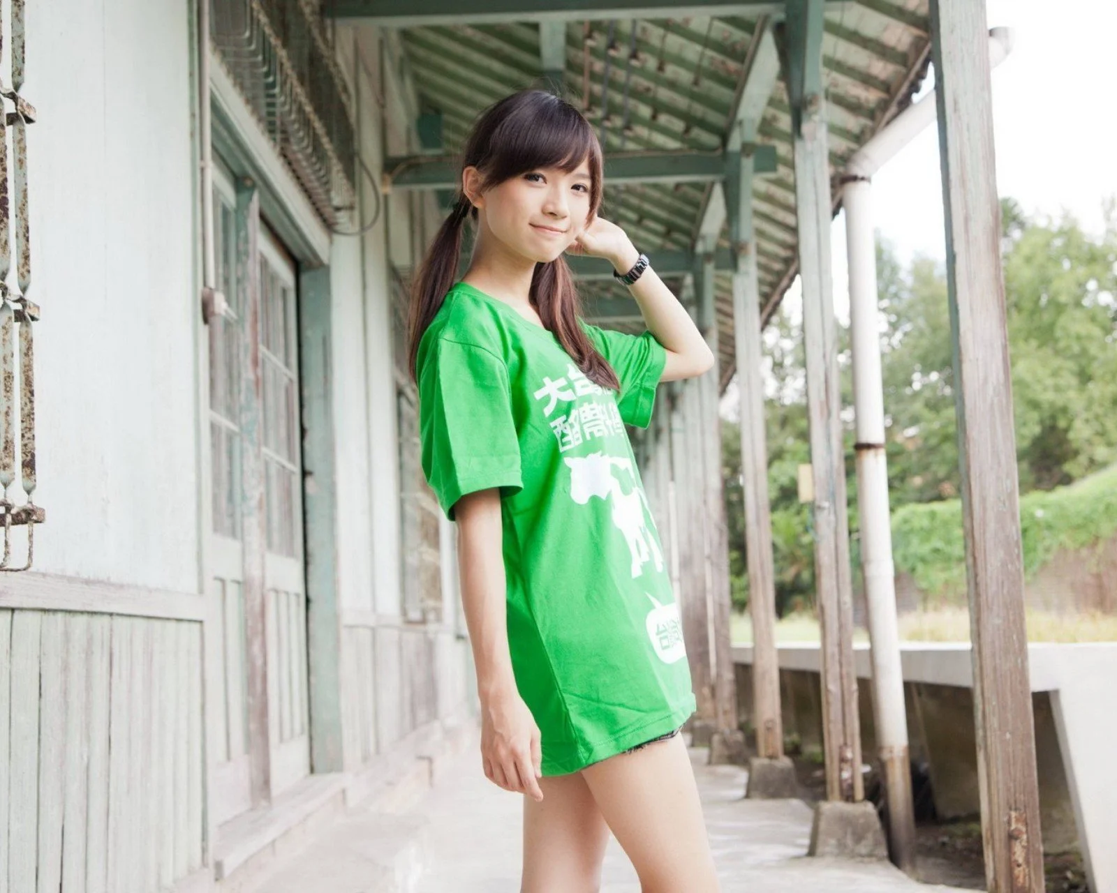 一名女子身穿绿色T恤站在带顶棚的户外走廊上。