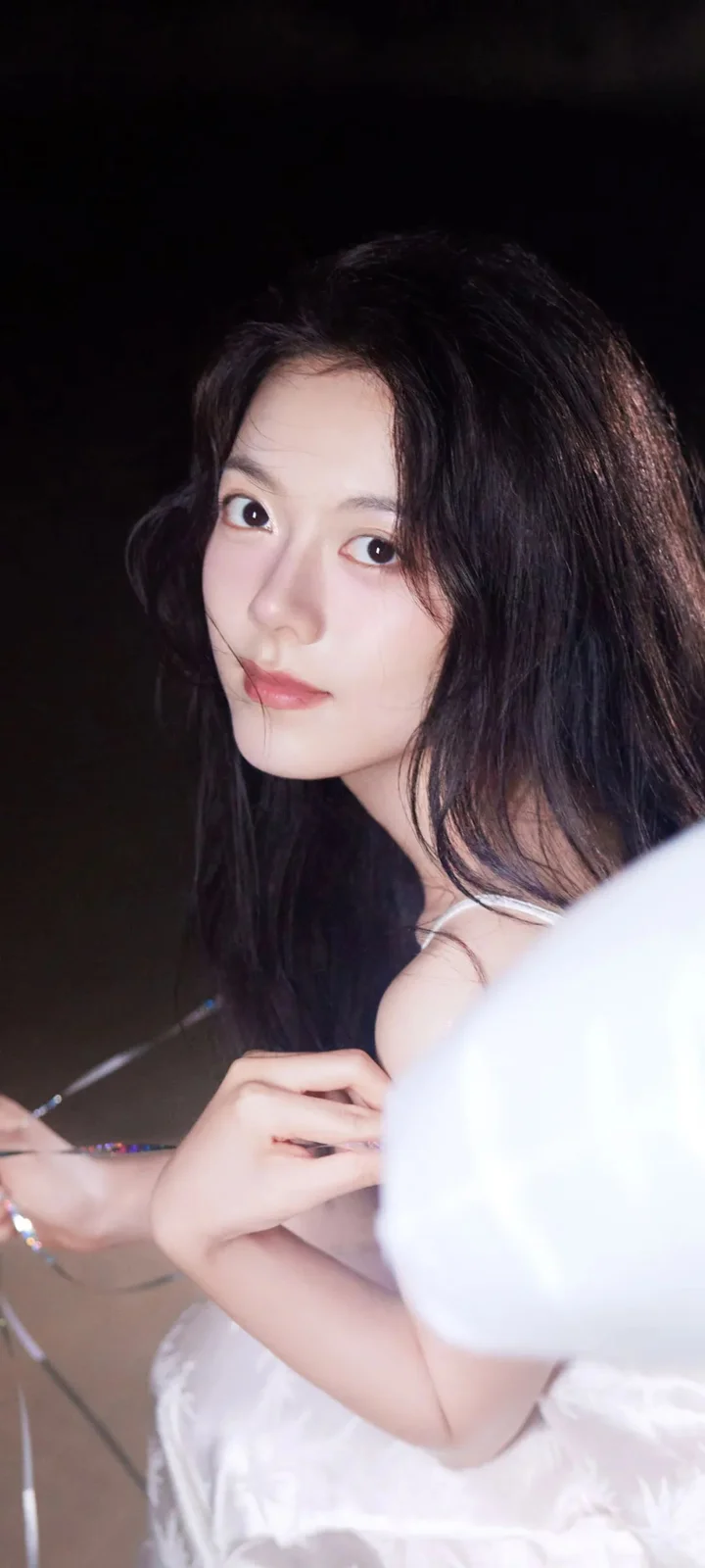一位长发女性在黑色背景前侧身看向镜头。