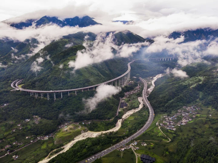 云雾环绕的青山之间，一条蜿蜒公路穿过山谷与村庄。