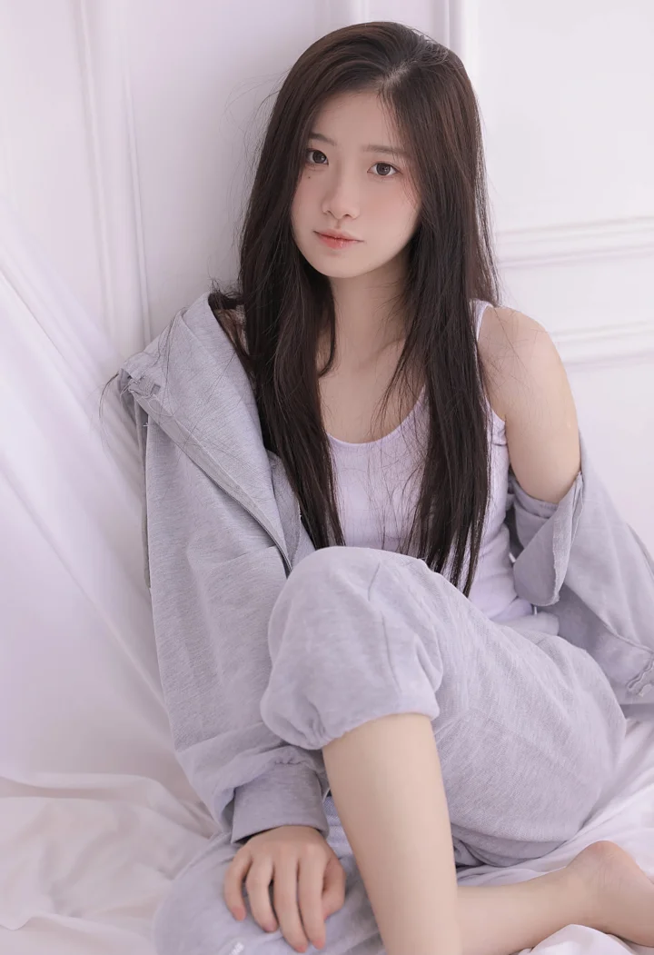 긴 머리의 여성이 연보라색 옷을 입고 밝은 실내 배경 앞에 앉아 있습니다.