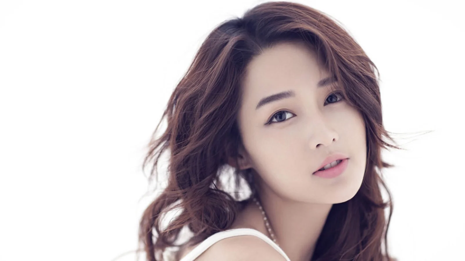 一位棕色长发女性在白色背景前面向镜头的近距离肖像。