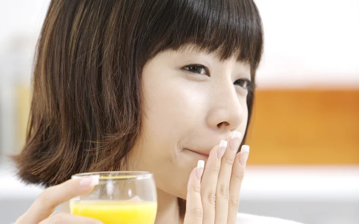 단발머리 여성이 오렌지 주스를 들고 손가락을 입술 가까이에 대고 있습니다.