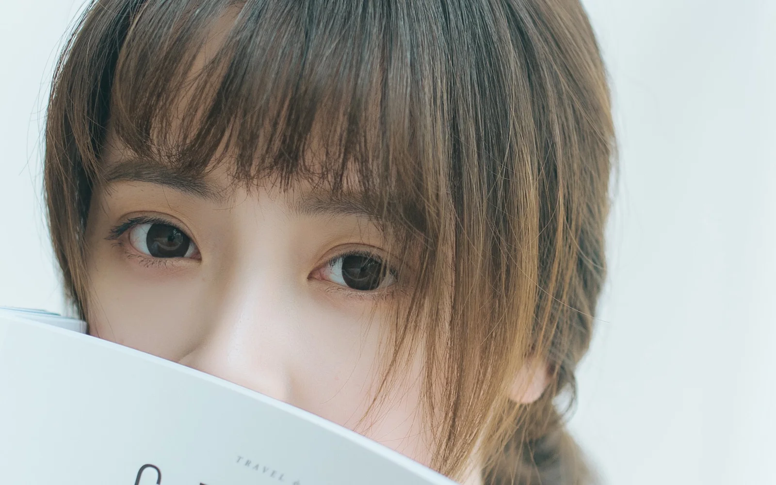 女性がカメラを見つめ、顔の下部を本で部分的に隠している。
