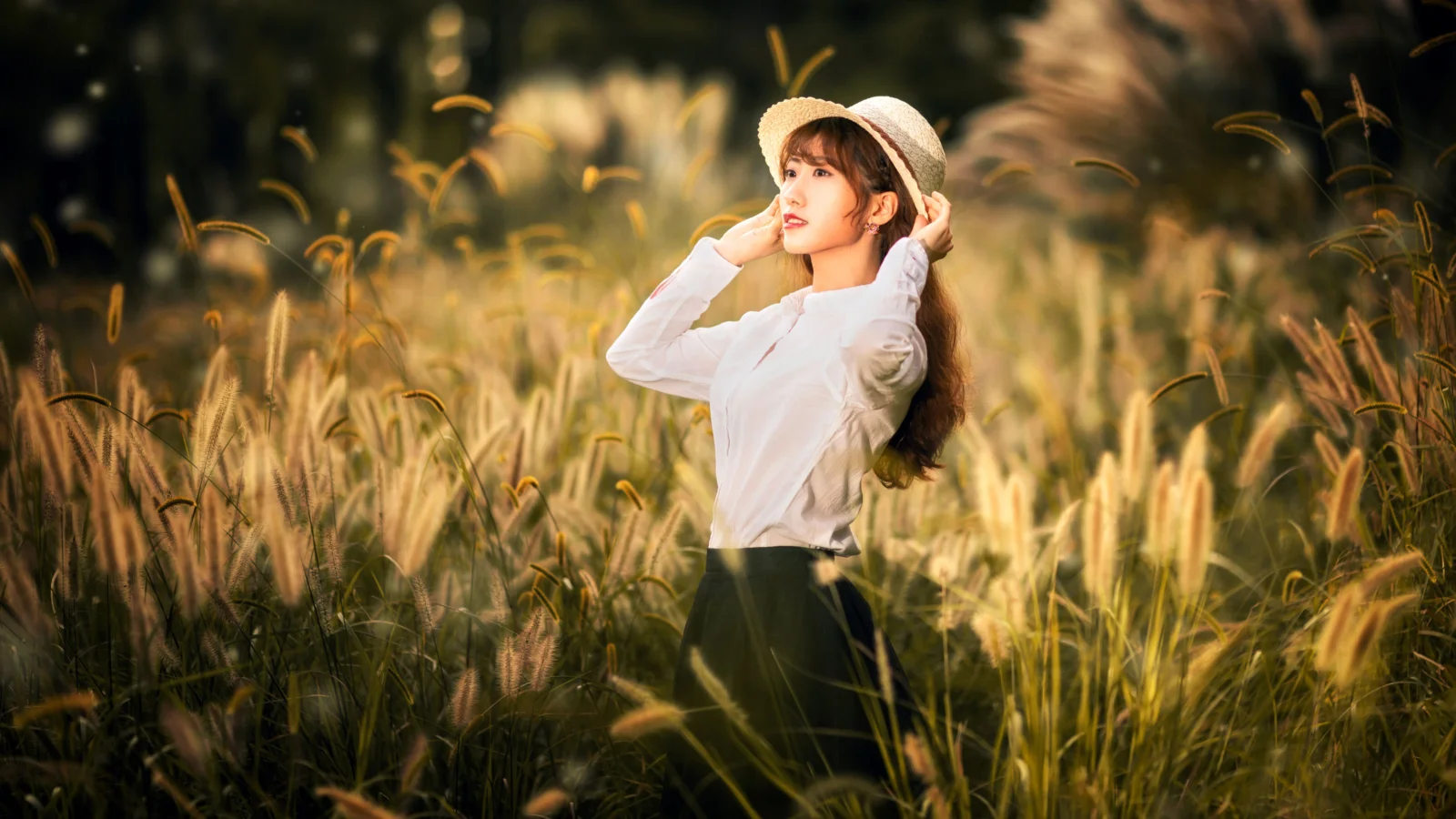 一名戴着草帽的女子站在阳光洒落的麦田中。