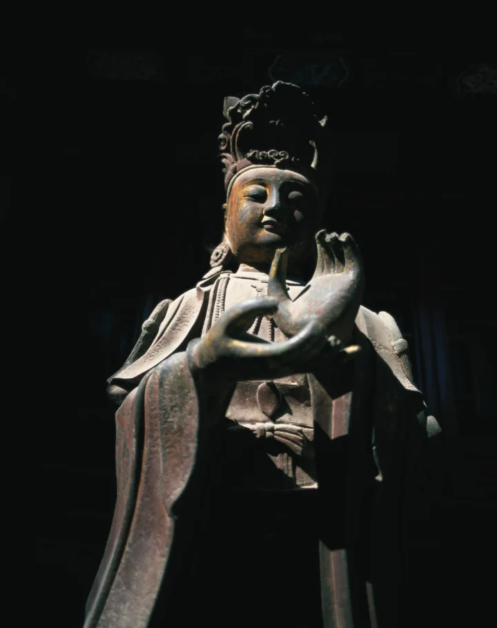 一尊古代雕像在黑暗背景前被侧上方光线照亮。