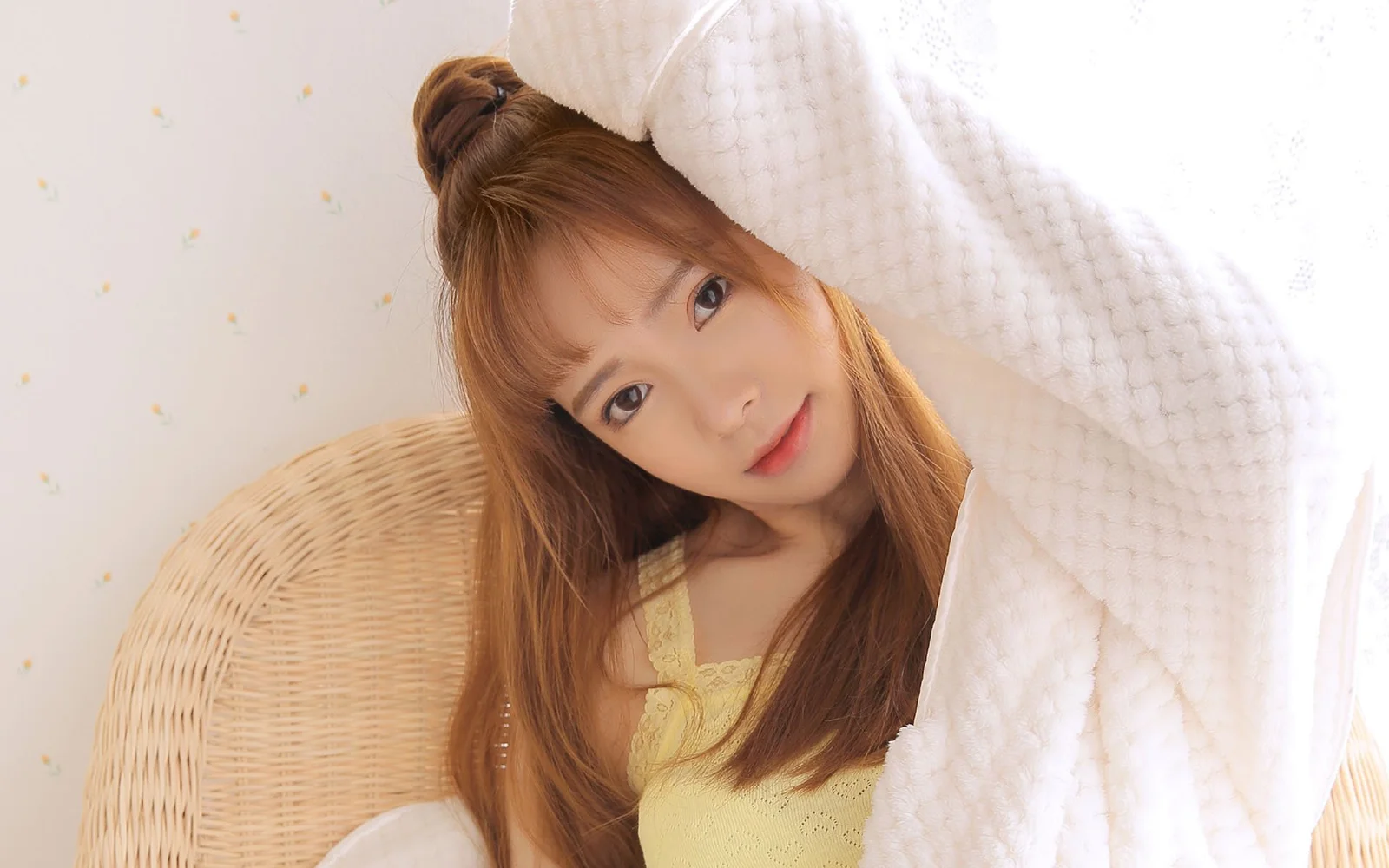 흰 담요를 두른 성인 여성이 라탄 의자에 앉아 카메라를 바라보고 있습니다.