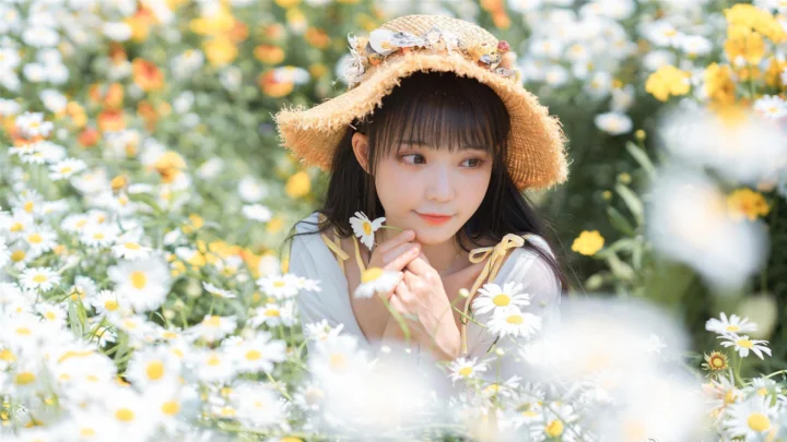 一名戴草帽的女子置身于开满白色和黄色花朵的花田中。