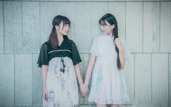 两位身穿连衣裙的女子站在木质墙面前并牵着手。