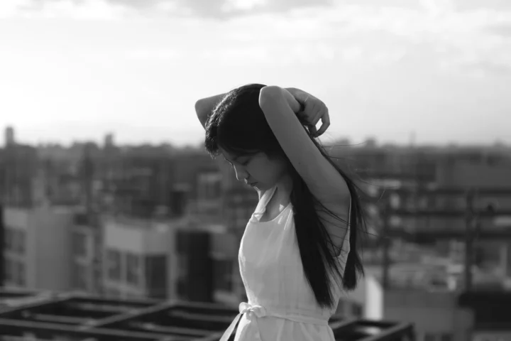 一名成年女子站在屋顶上整理长发，背景是虚化的城市建筑群。