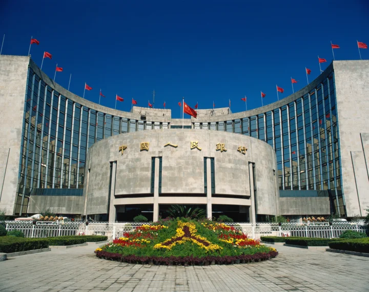 一座弧形城市建筑前立有许多红旗，入口前装饰着彩色花坛。