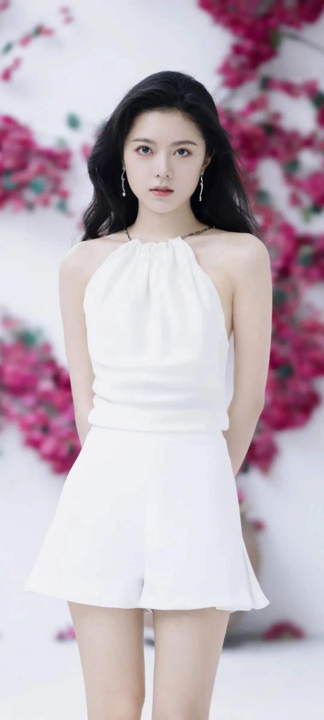 白いドレスを着た女性が、ピンクの花を背景に立っている。
