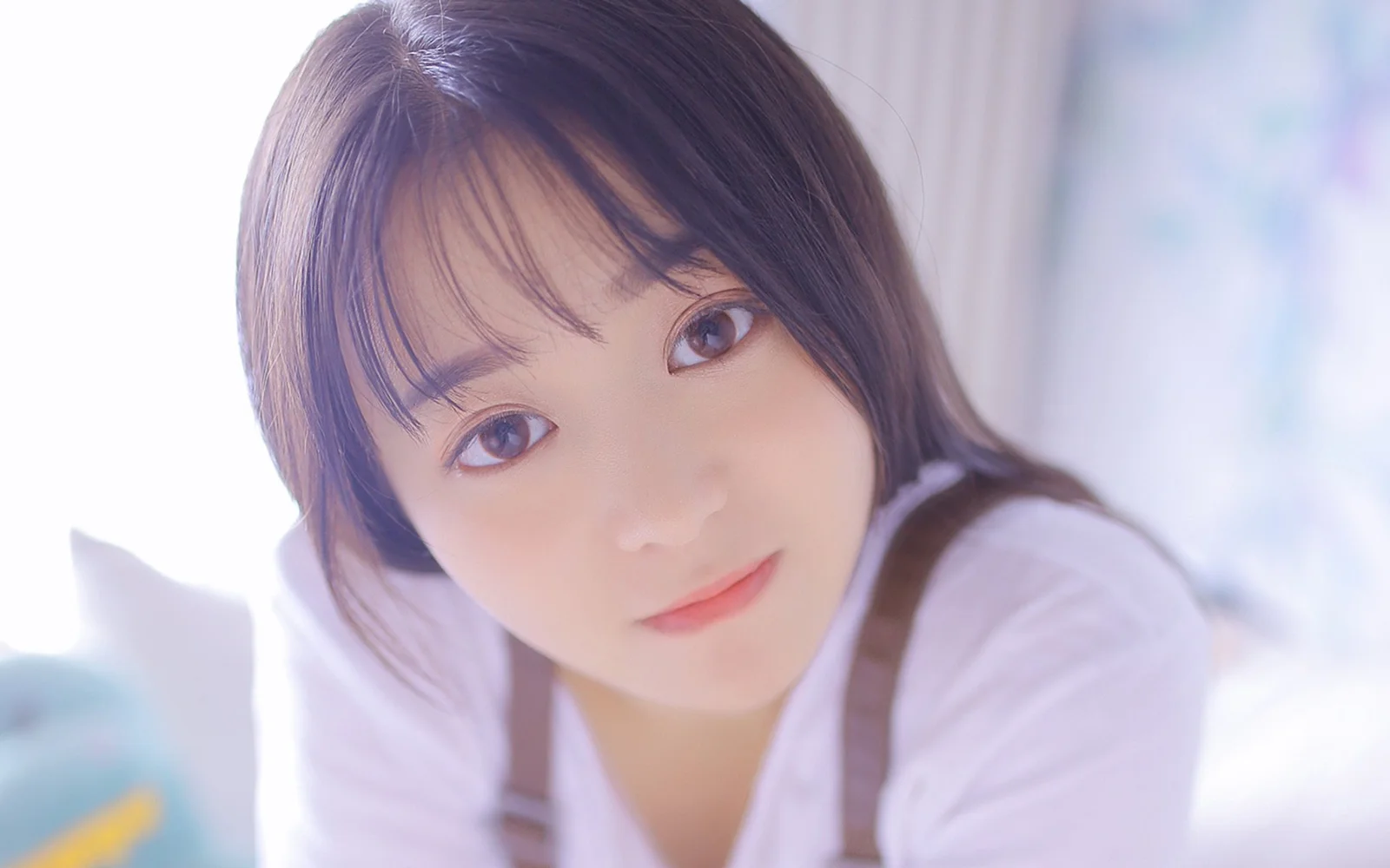 茶色の短い髪の女性が、柔らかく明るい室内の光の中でカメラの近くに寄って微笑んでいる。