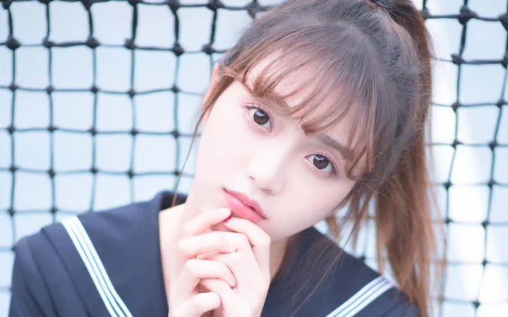 격자형 펜스를 배경으로 갈색 긴 머리 여성이 카메라를 바라보는 클로즈업 인물 사진입니다.