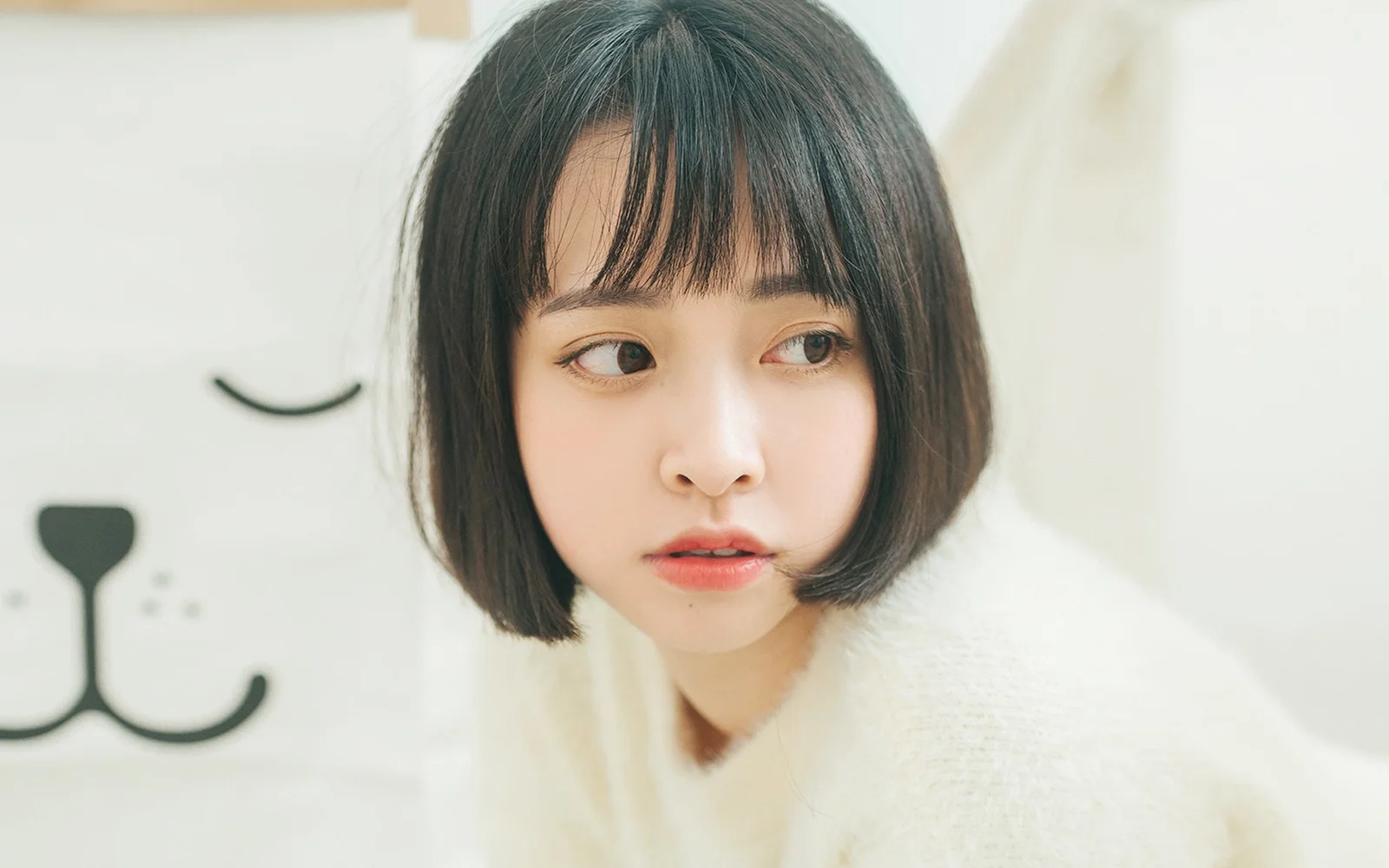 一名留著齊耳短髮的女生穿著淺色毛衣，側頭望向畫面右側。