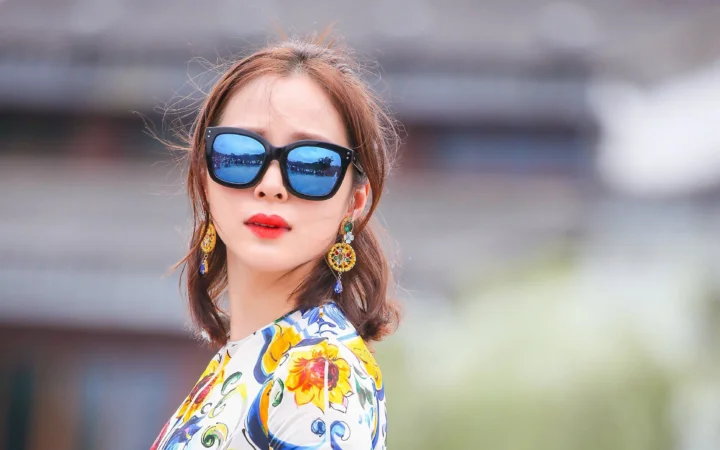 一位戴着墨镜、佩戴彩色耳饰并穿着花卉图案上衣的女性面对镜头。