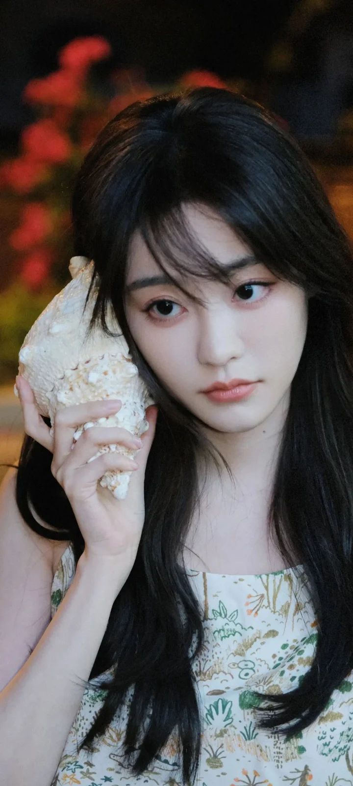 一名长发女子手持贝壳靠近脸侧，背景虚化。