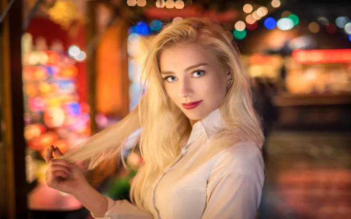 一名身穿白色上衣的金发女子在彩色虚化灯光前回望镜头。