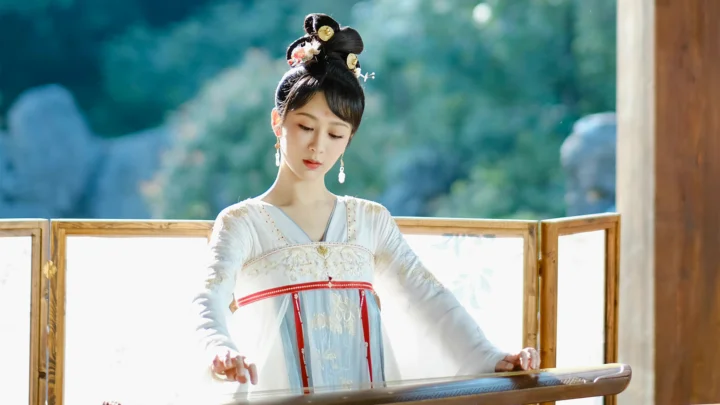 一名身穿传统服饰的女子站在窗前弹奏古筝，背景是柔和的绿色景色。