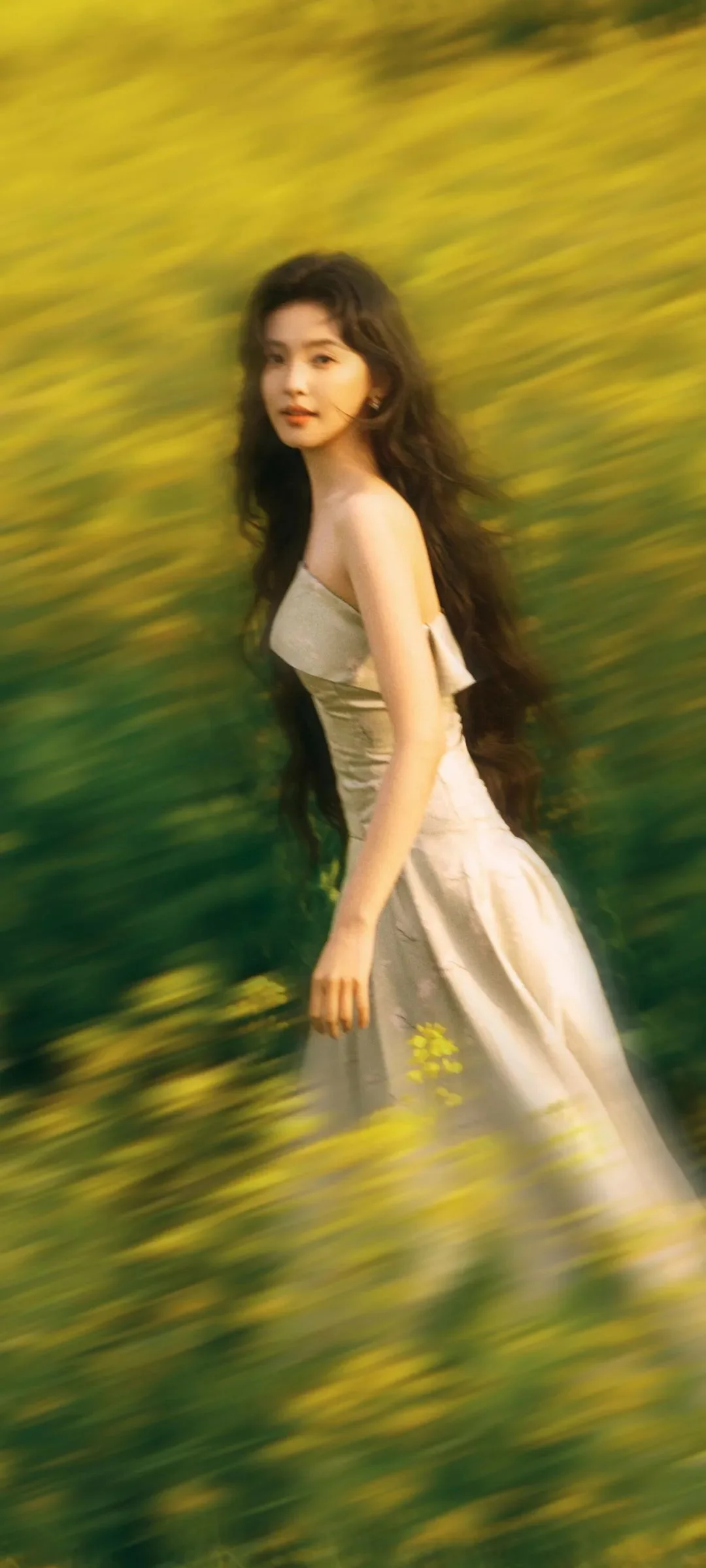 연한 색 원피스를 입은 여성이 금빛과 흐릿한 녹색 배경 앞에 서 있습니다.