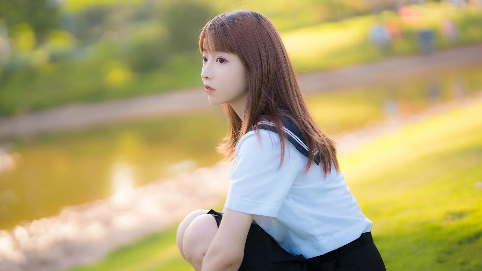 一名长发女子坐在阳光柔和的公园草地旁。