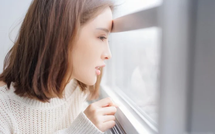 성인 여성이 창가에 서서 옆모습으로 바깥을 바라보고 있다.