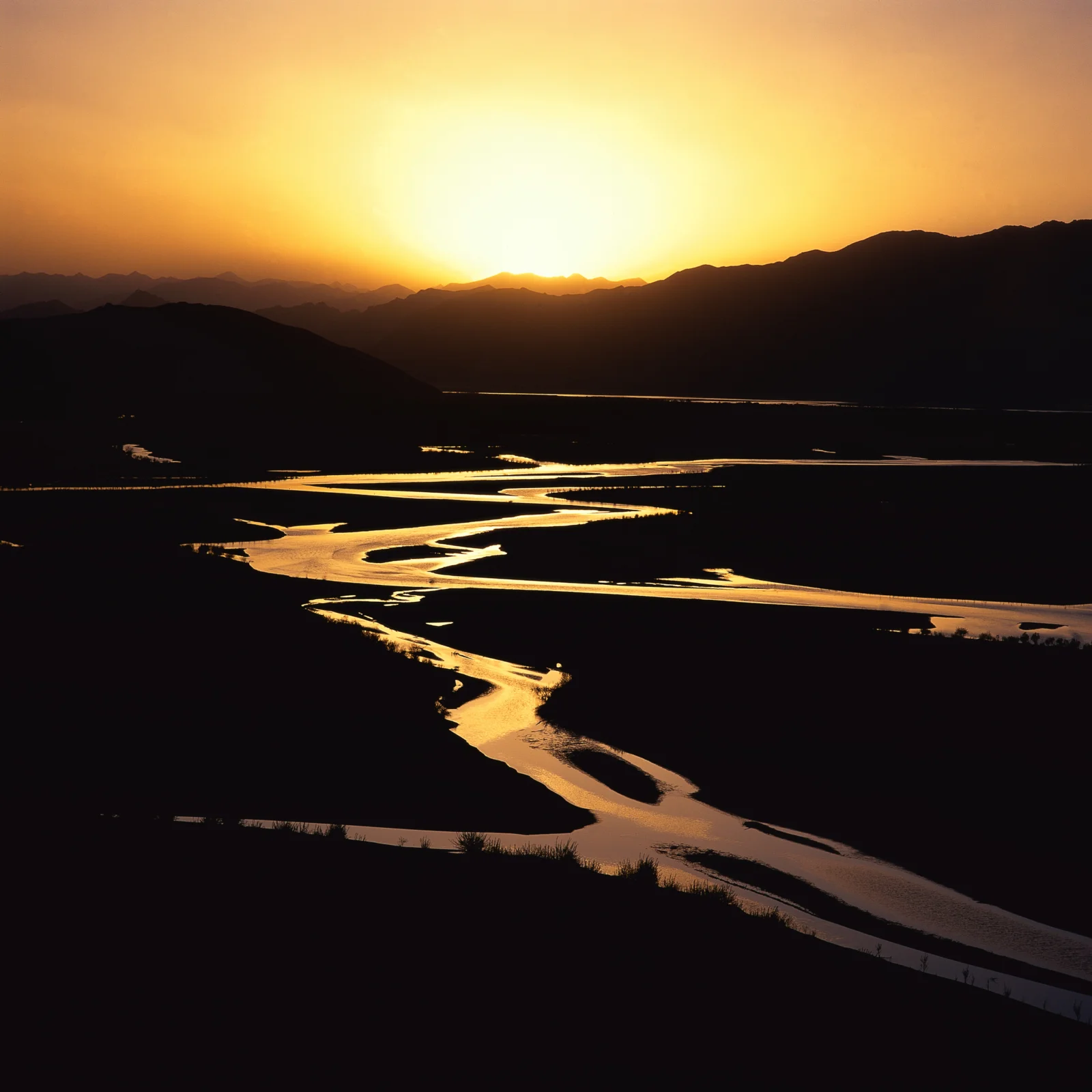 夕阳映照群山与蜿蜒河流，形成金色而深沉的自然景观。